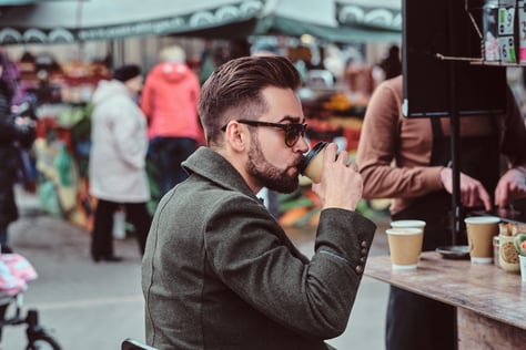 modern-elegant-man-sunglasses-is-drinking-coffee-while-sitting-outside-coffeeshop